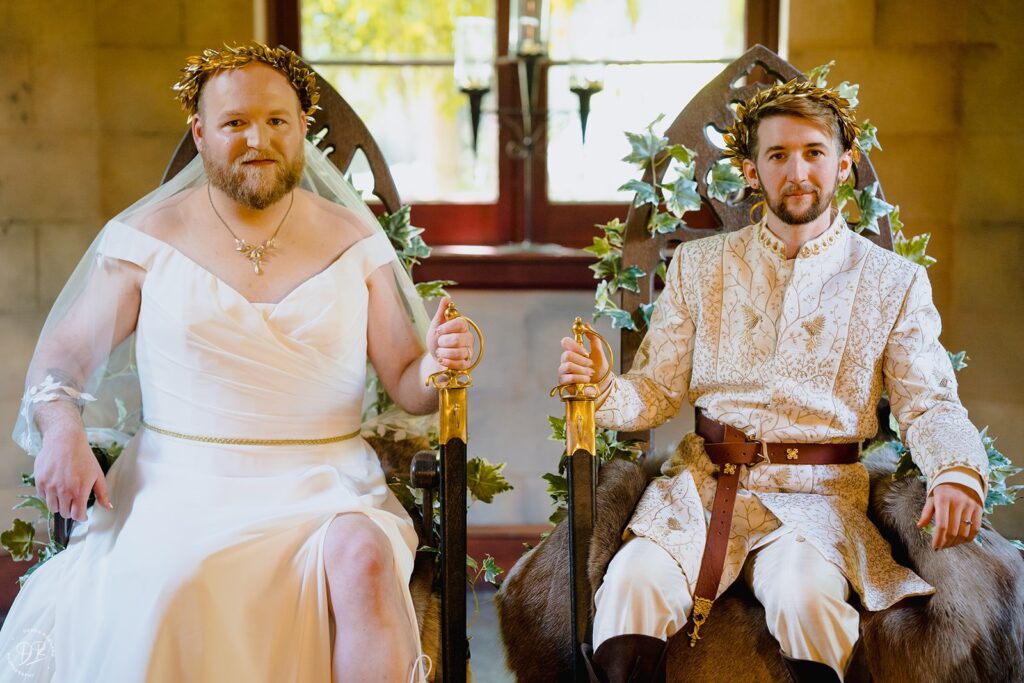 A newlywed couple sitting in grand chairs next to each other smiling 
