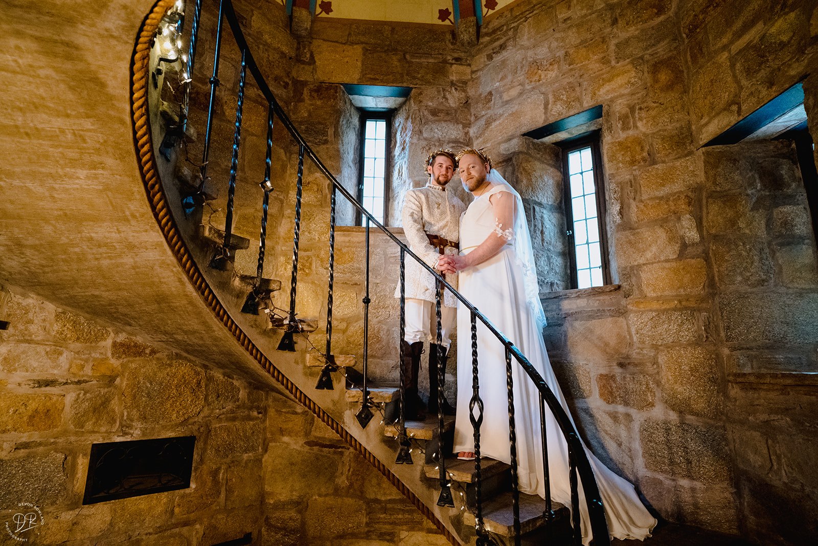 A newlywed couple standing on a spiral staircase inside of a stone building during their Cloisters Castle wedding.