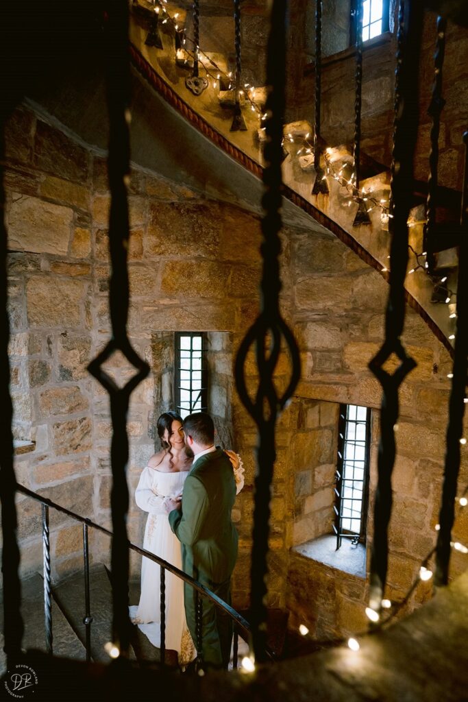 View of a newlywed couple with their arms around each other seen through an iron staircase railing 