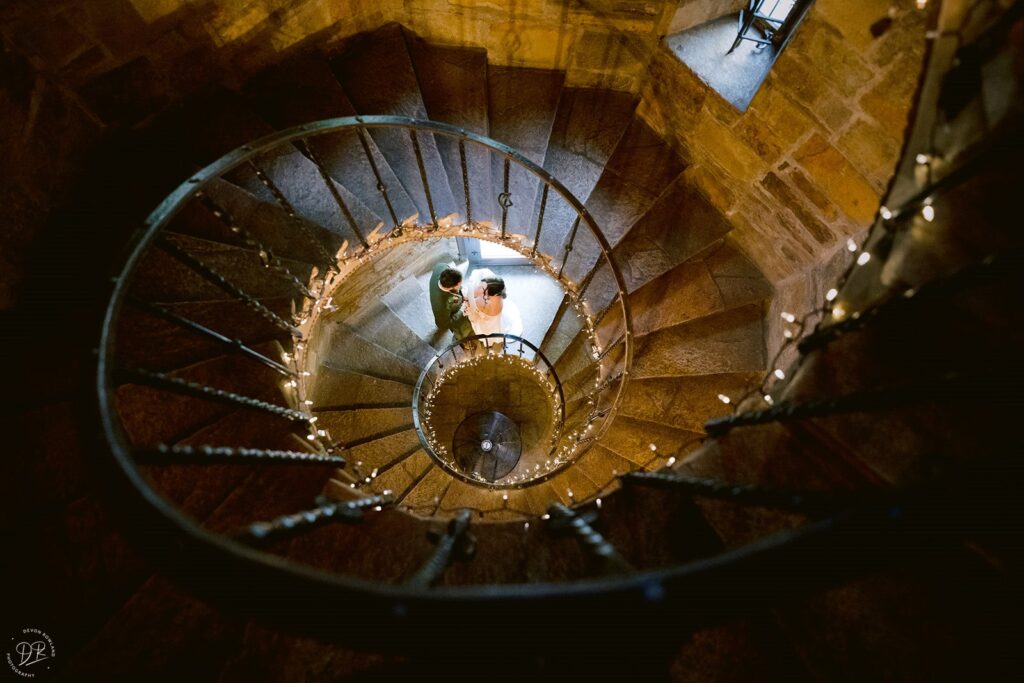 View looking down a spiral staircase of a newlywed couple standing close. 