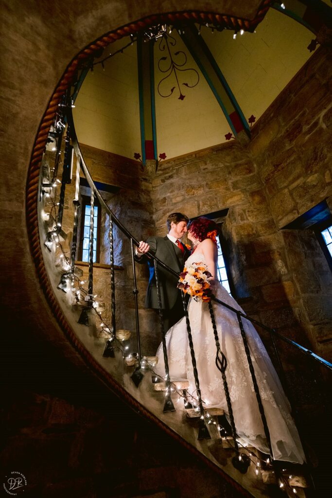 A couple standing on a spiral staircase lined with fairy lights 