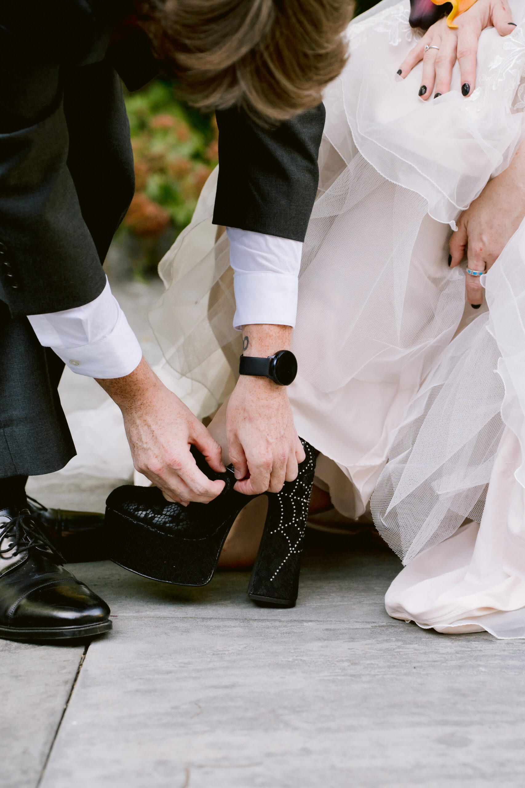 man in a tuxedo helping woman in a wedding dress fix her shoe