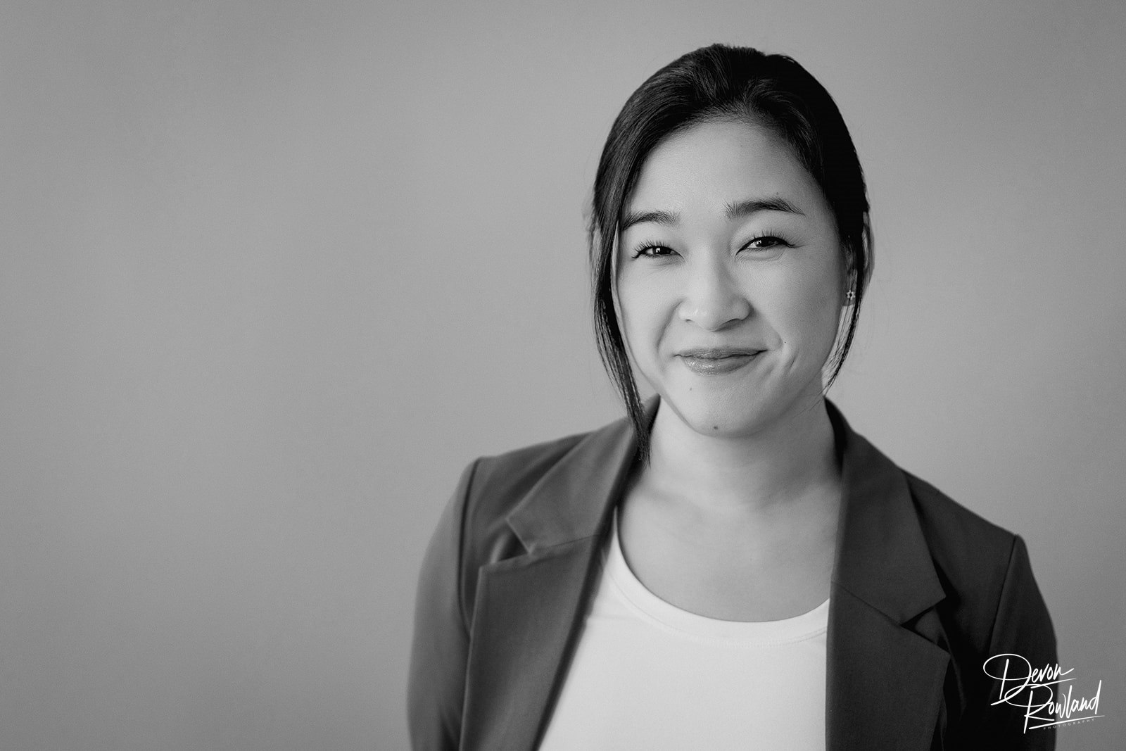 A Korean woman who is smiling wearing a white shirt and a blazer