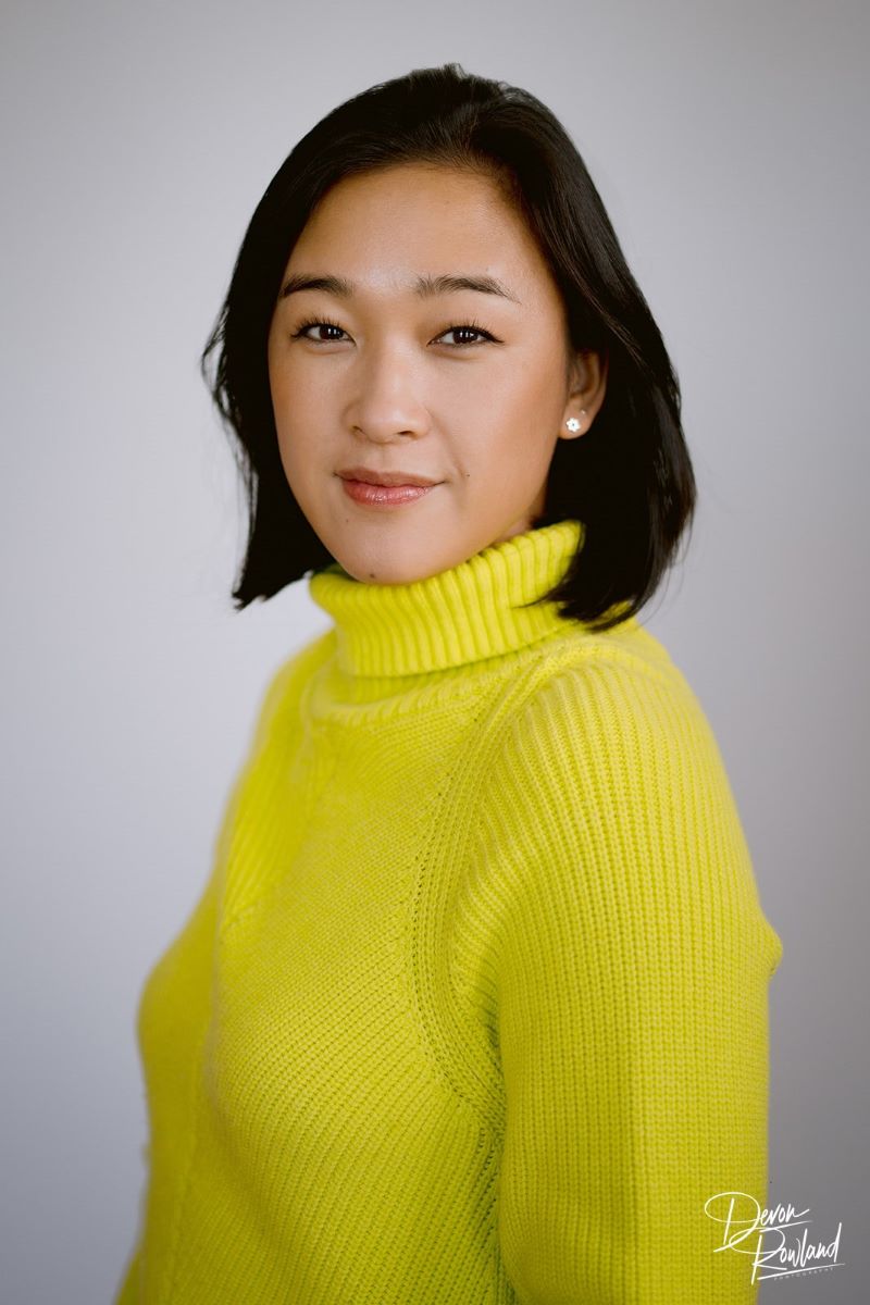 A Korean woman in a yellow turtleneck sweater looking towards the camera and softly smiling 