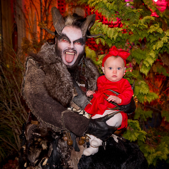 Baby in red dress and bow looks stunned while sitting on Krampus's lap.