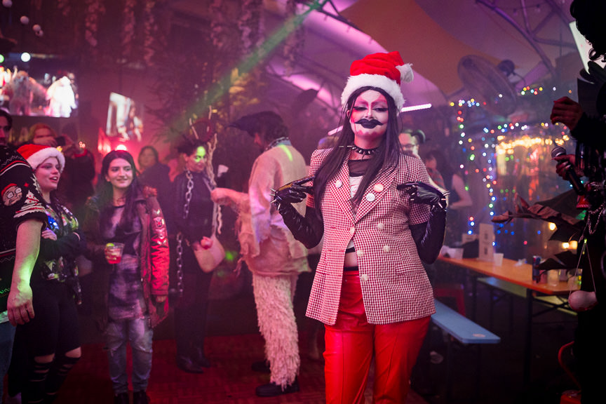 Goth drag Santa Krampus takes the stage on a festive and hazy dance floor.