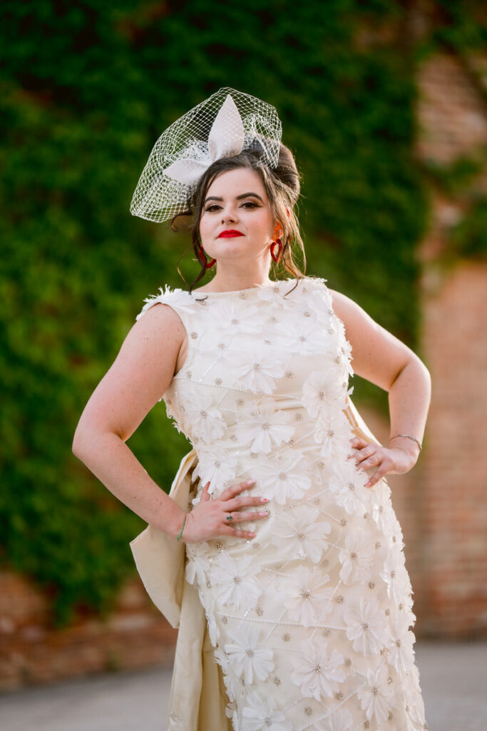 A person in a wedding dress smiling with their hands on their hips 