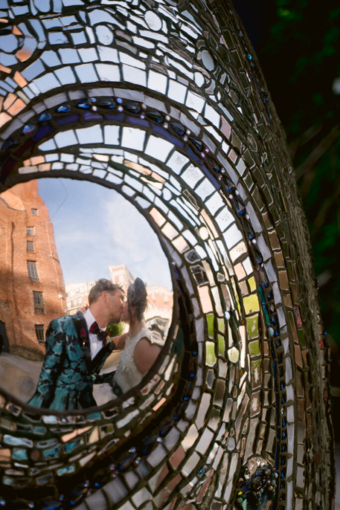 The reflection in a sculpture of a newlywed couple kissing 