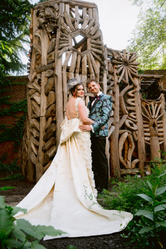 A newlywed couple posing in front of a wooden sculpture in a garden during their American Visionary Art Museum wedding 