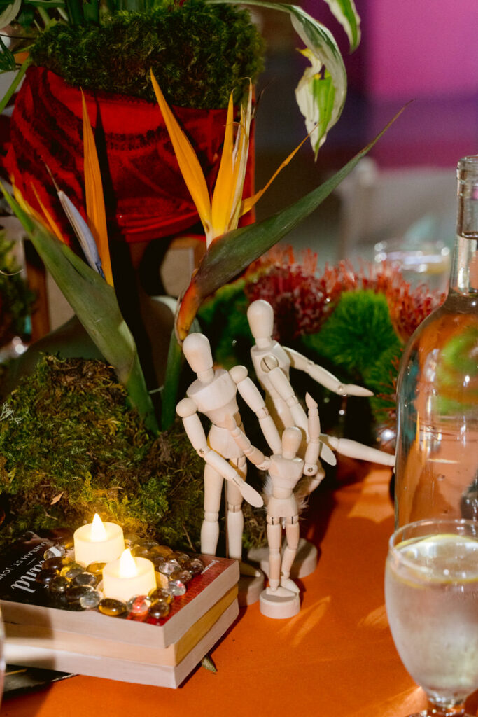 Small wooden mannequins on a wedding reception table with other flowers and candles. 