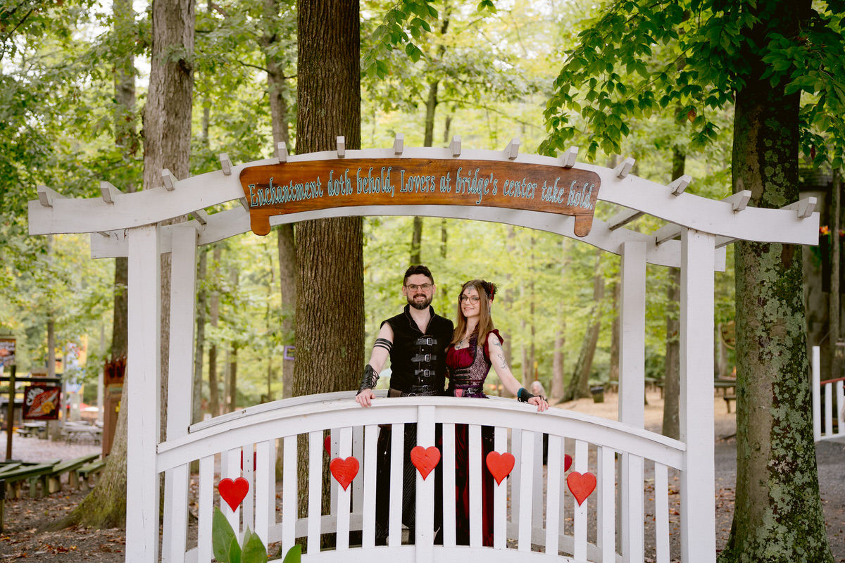 A couple standing on a small wooden bridge dressed up in costumes at their Renaissance Festival wedding