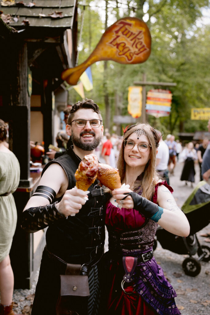 A newlywed couple cheersing with turkey legs at their Renaissance Festival wedding 