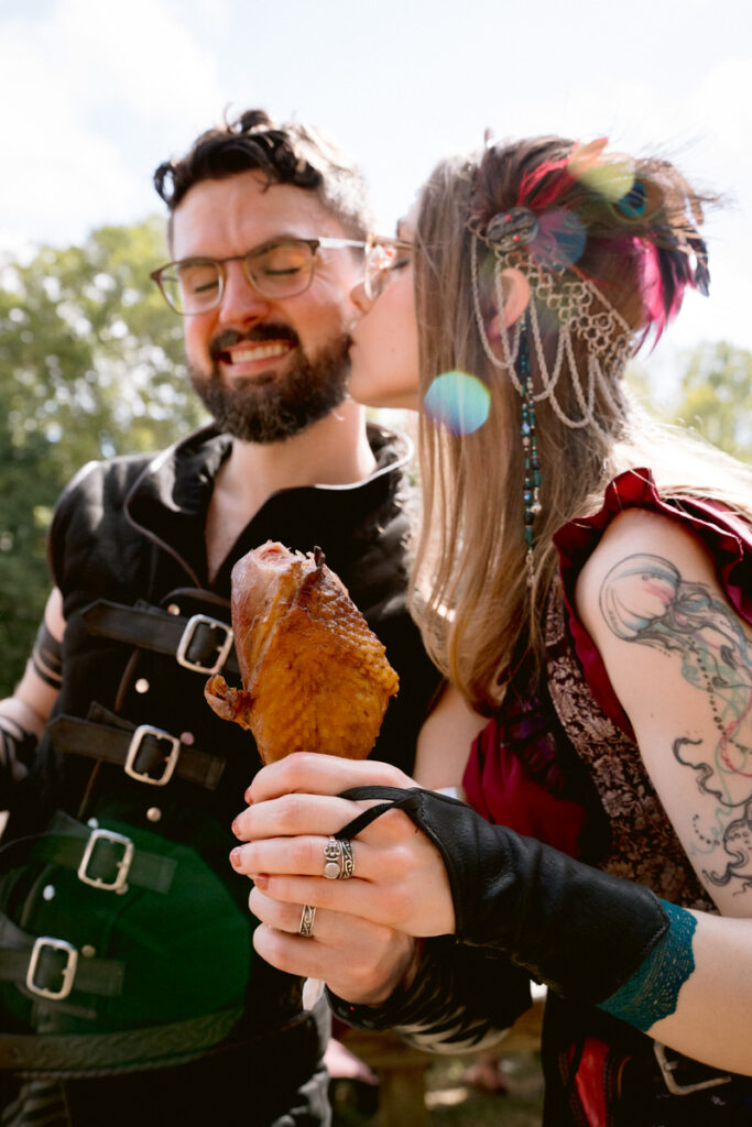 A person kissing their partner's cheek as they hold out a turkey leg and show off wedding rings 
