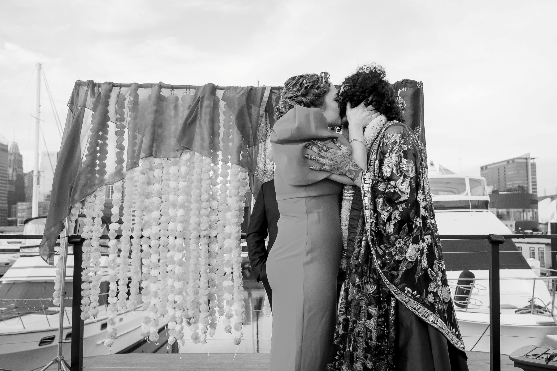 a couple kissing on a deck in a harbor behidn them is a colorful arch for their wedding ceremony 