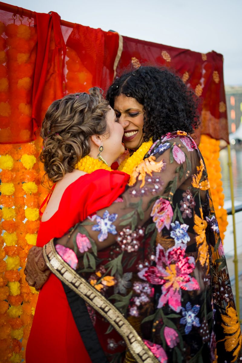 a couple smiling and hugging each other one woman is wearing a colorful kimono and yellow lei the other woman is wearing a red dress and yellow lei 