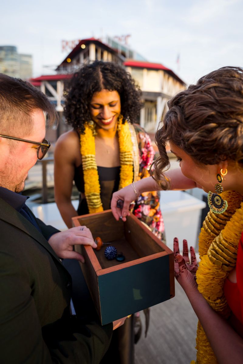 an officiant at a wedding ceremony holding a box and one woman is lifting an object out of the box as her partner watches 